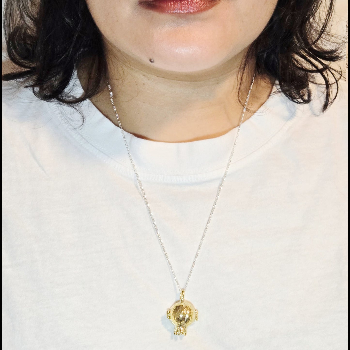 Close-up of a person wearing a gold necklace with a pendant on a plain background