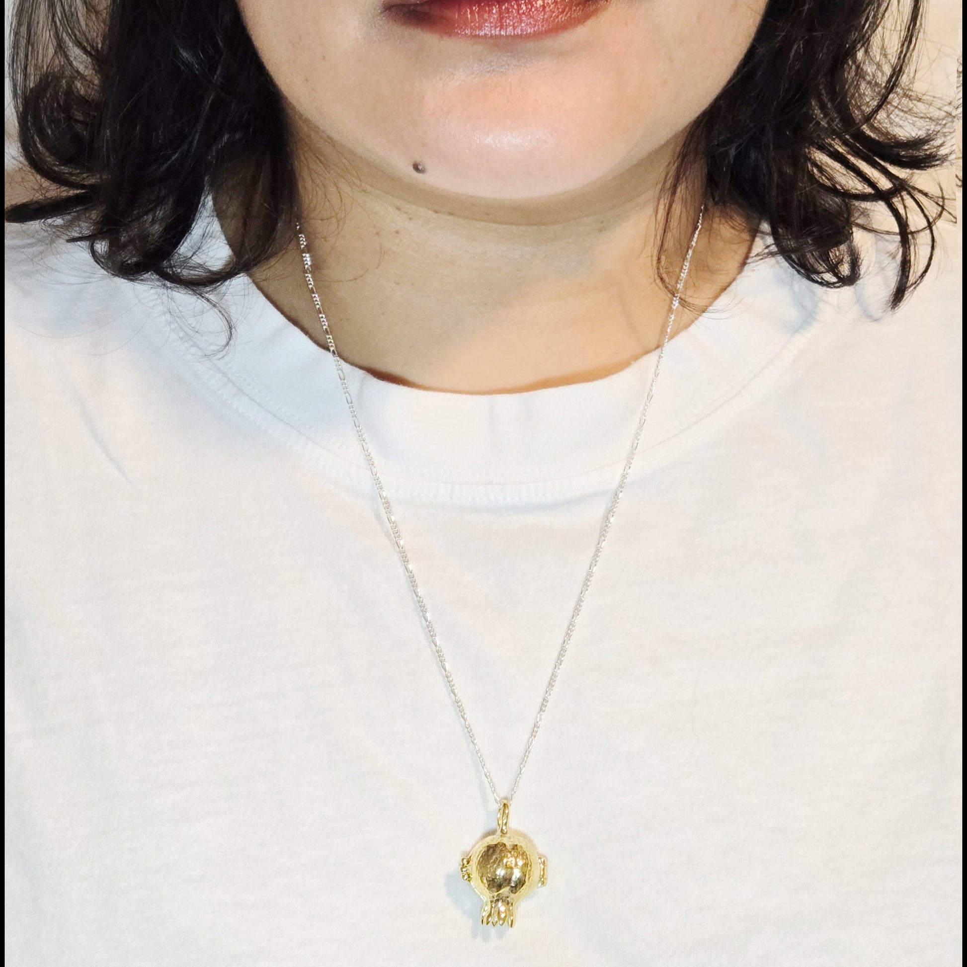 Close-up of a person wearing a gold necklace with a pendant on a plain background